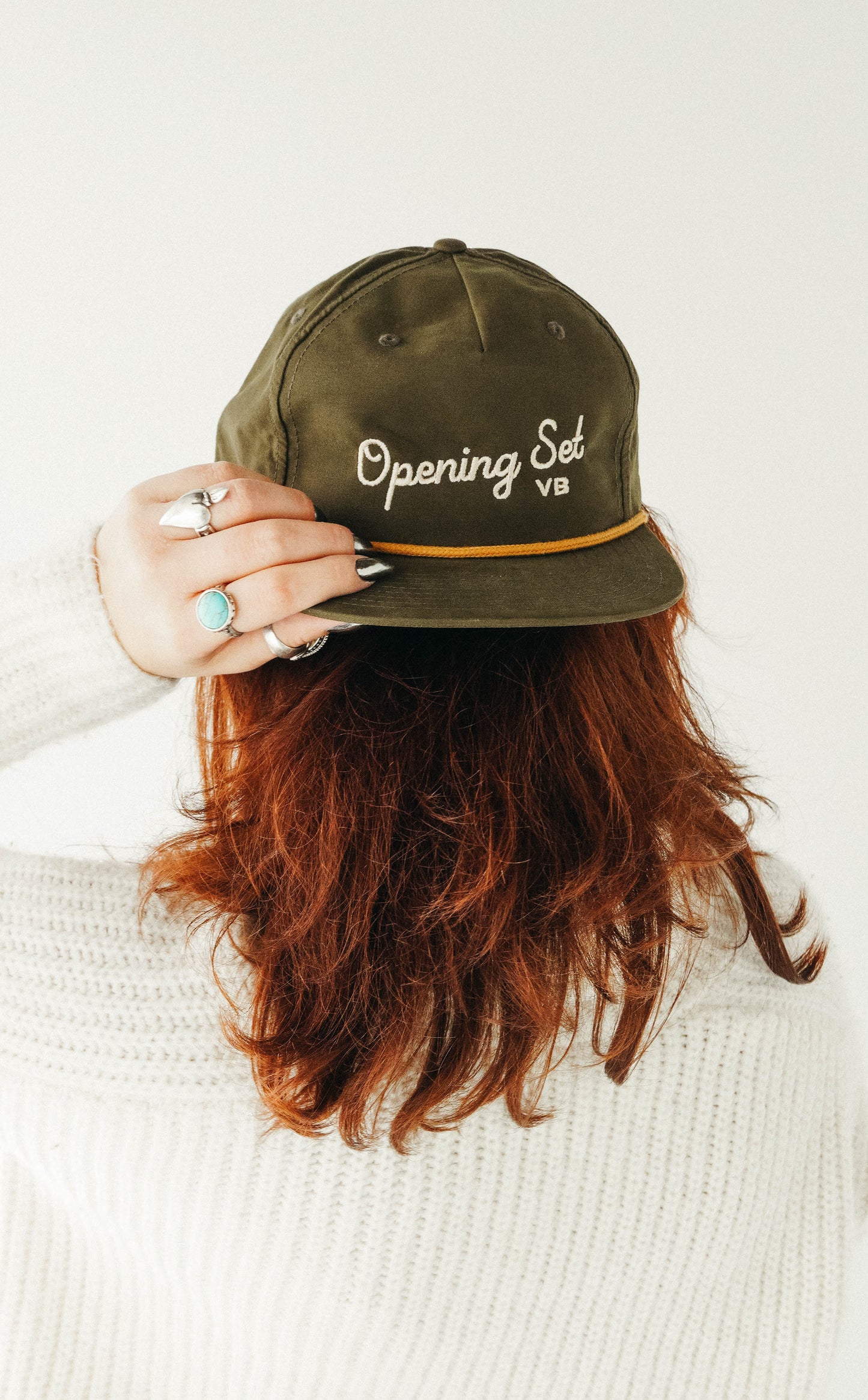 Person wearing an olive green cap with 'Opening Sal' text on a white background