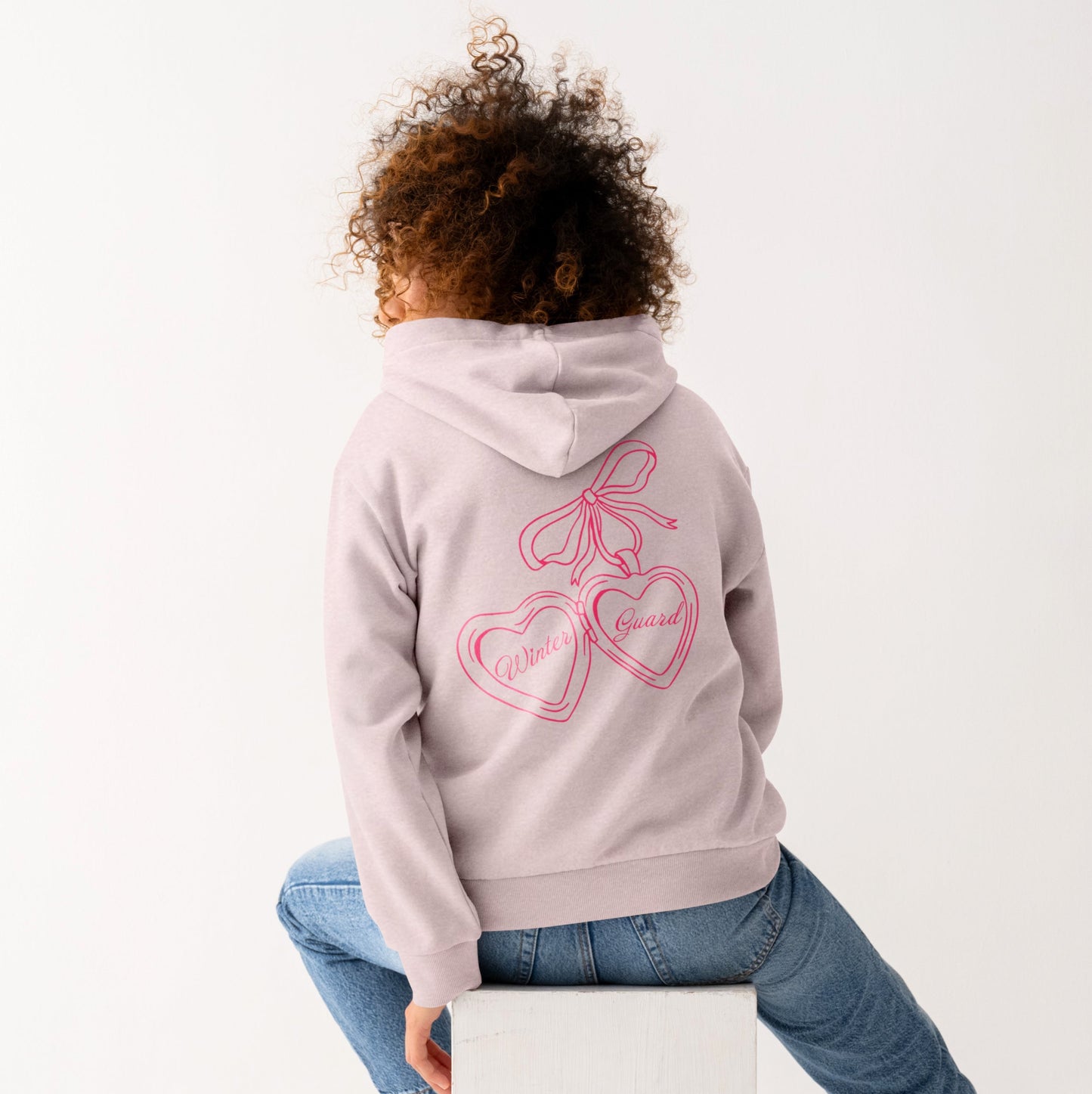 Person wearing a pink hoodie with a logo, sitting on a white cube against a white background